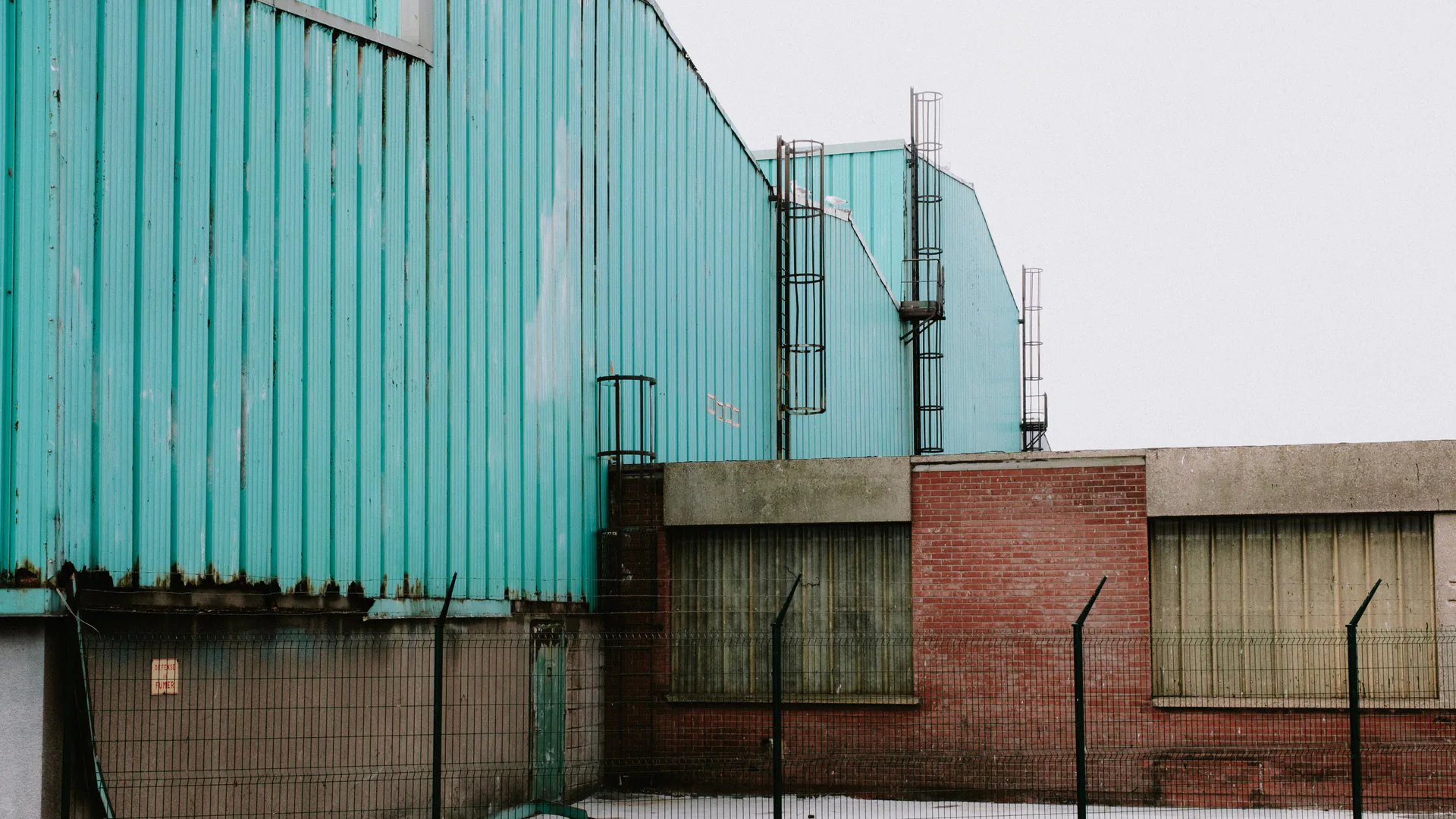 Green-clad industrial buildings behind a metal perimeter fence